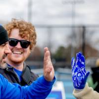 Louie high fives an alum in a winter hat while another alum laughs